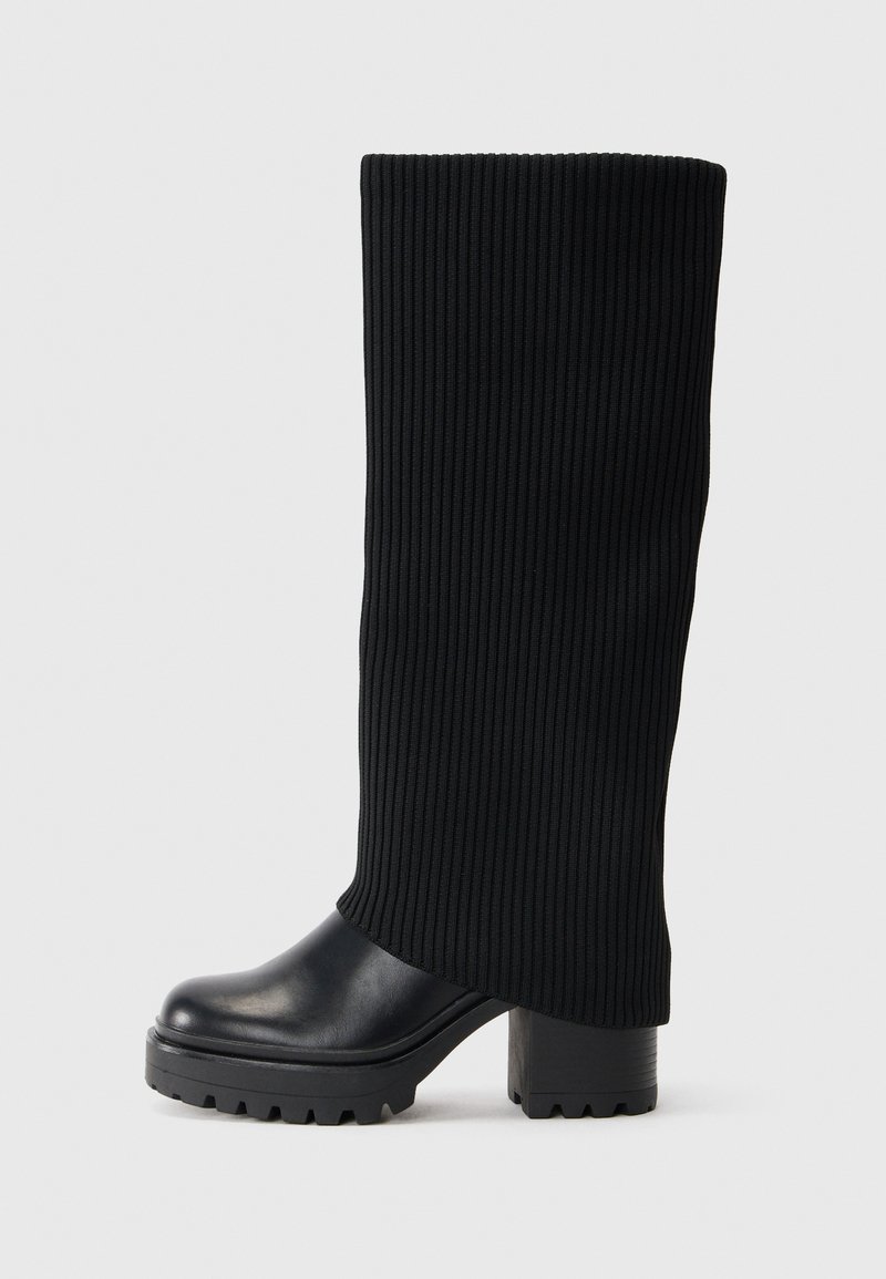 Black knee-high boots with a ribbed fabric shaft, chunky rubber sole, and a block heel. Smooth leather toe with a rounded shape.