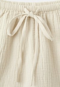 Pantalon en tissu beige texturé avec une ceinture élastique et un nœud de cordon en tissu noué au centre devant.