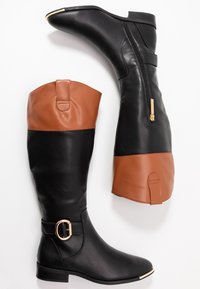 Botas altas de cuero negro y marrón con cremallera lateral y detalle de hebilla dorada, colocadas de forma plana sobre un fondo blanco.