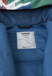 Unutrašnjost plave, podstavljene jakne s oznakom "reima" i uputama za njegu. Istaknute boje: zelena, crvena, bijela na vanjskom materijalu.