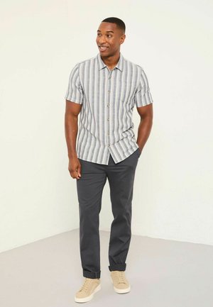 Kurzärmeliges gestreiftes Hemd in Blau und Weiß mit Kragen und Knopfleiste, kombiniert mit grauen Chinos und beigen Sneakern.