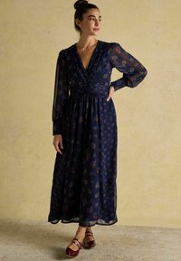 Tumesinine lilleline kleit pikkade läbipaistvate varrukatega, V-kaelusega ja kitsas talje, voolava seeliku ja peente voldi detailidega.