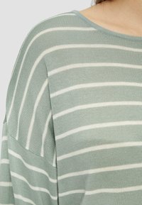 Pull rayé vert clair avec des rayures blanches horizontales, texture tricotée, encolure dégagée et couture d'épaule tombante.