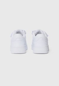 Baskets blanches avec une tige en cuir lisse, un col rembourré et un laçage à l'avant. Semelle en caoutchouc texturé avec une marque minimale sur le talon.
