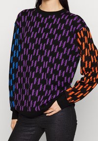 Maglione nero con un motivo a zigzag in viola, blu e arancione. Maniche lunghe, polsini e colletto a coste con una vestibilità rilassata.