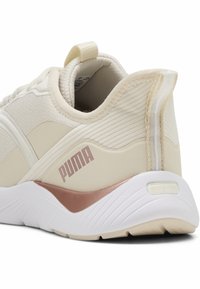 Zapatilla deportiva beige con parte superior de tela texturizada, suela de goma y detalles en dorado rosa. Presenta un tirador en el talón y el logo de Puma en el lateral.