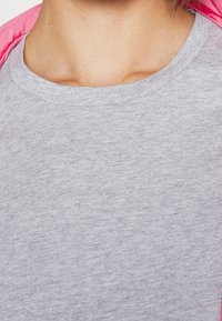 Grijze katoenen t-shirt met een ronde halslijn, met een gladde textuur en een minimaal gemêleerd patroon. Een gedeeltelijk zicht op een roze jas is ook zichtbaar.