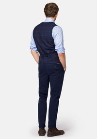 Granatowa kamizelka w kratkę z brązowymi akcentami, zestawiona z jasnoniebieską koszulą i ciemnymi spodniami. Brązowe botki za kostkę dopełniają całość.