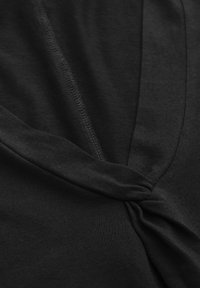 Schwarzes Strickoberteil mit einer verdrehten Detail vorne, glatter Textur und dezenten Nähten entlang der Kanten.