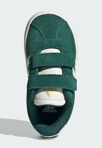 Sneaker verde in suede con cinturini in Velcro bianchi, punta arrotondata e logo dorato Adidas sulla linguetta. Dettagli testurizzati caratterizzano il design.