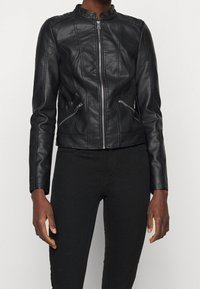 Giubbotto di pelle nera con un design accorciato, chiusura con zip, colletto alto e dettagli di cucitura verticale. Include due tasche laterali con zip.