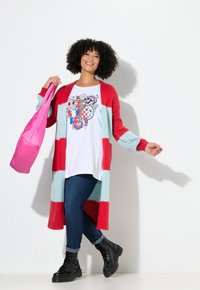 Langes Cardigan mit roten und hellblauen Streifen, weißes T-Shirt mit Grafik, blaue Jeans, schwarze Schnürstiefel und eine pinke Umhängetasche.