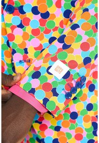 Giacca da abito a pois colorati con bottoni blu, polsini rosa e etichetta logo. Presenta cerchi vivaci in rosso, verde, giallo e blu.