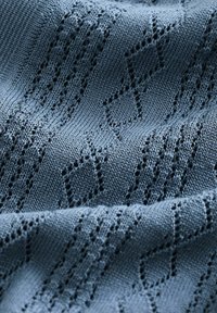 Dzianina w ciemnym niebieskim kolorze z diamentowym wzorem; cechuje się otwartym splotem dla tekstury i przewiewności; gładkie wykończenie i miękki układ.