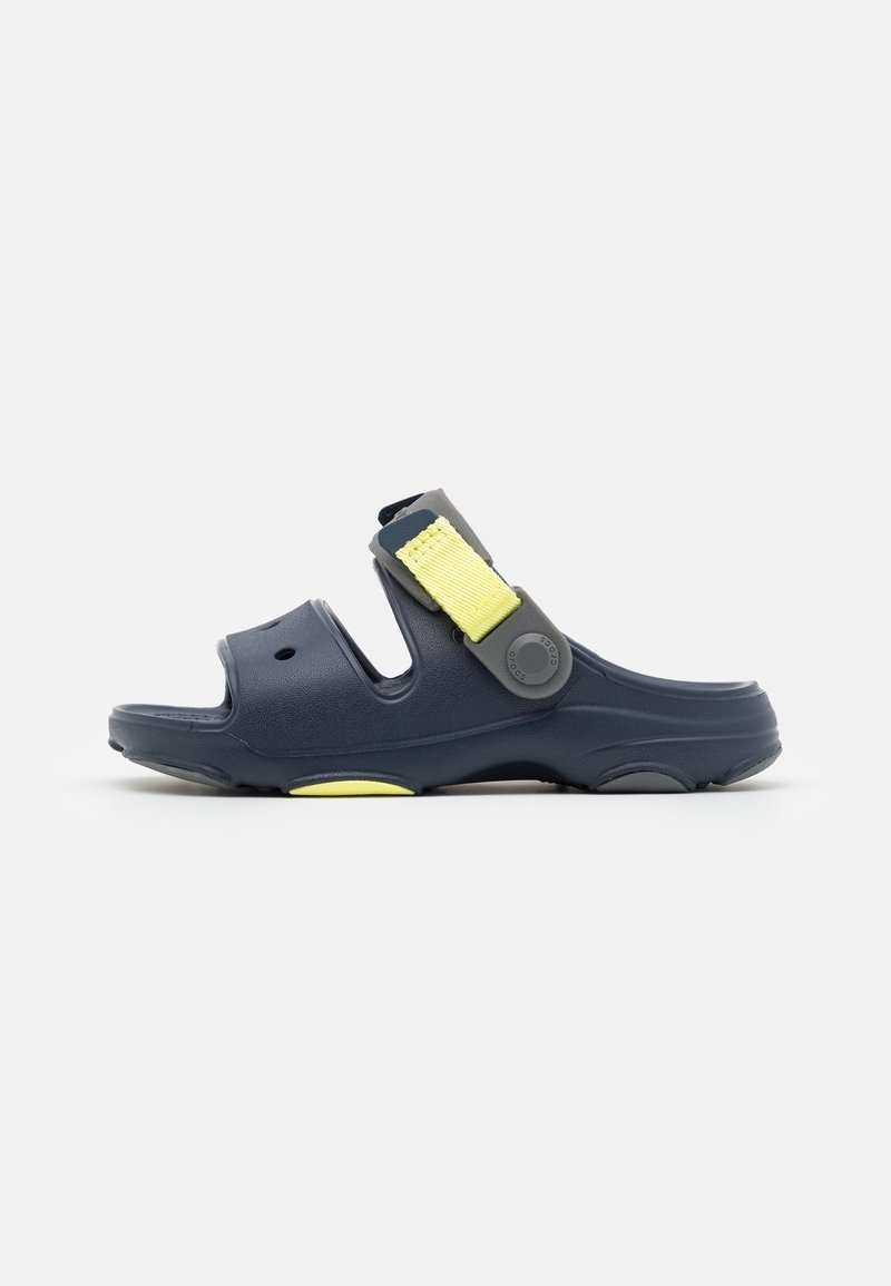 Sandale bleu marine à enfiler avec deux larges découpes et une sangle jaune ajustable sur le dessus du pied, présentée sur un fond blanc.