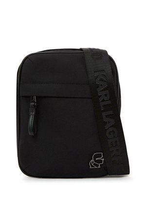 Čierna crossbody kabelka s predným vreckom so zipsom, hrubým popruhom s plastickým nápisom „KARL LAGERFELD“ a kovovým detailom loga v dolnom rohu.