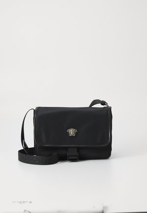 Borsa messenger nera in nylon con un design strutturato, dotata di una chiusura a forma di testa di leone argentata, tracolla regolabile e dettagli sulla tracolla con logo in rilievo.
