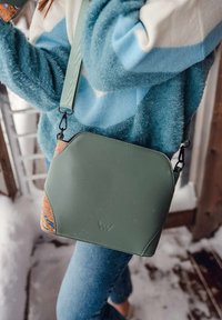 Zelená křížová taška s texturovanými korkovými detaily, černým kováním a zaobleným designem. Měkká tkanina, čisté linie a nastavitelný popruh.