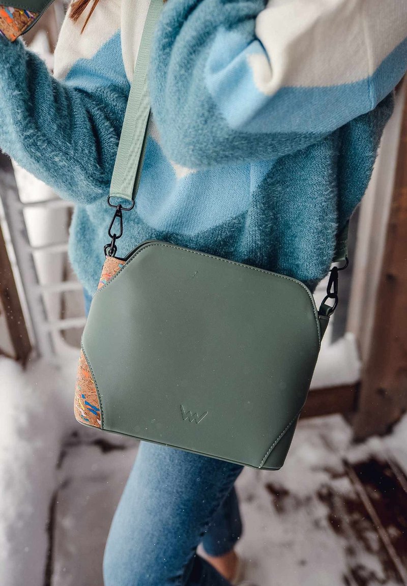 Zelená křížová taška s texturovanými korkovými detaily, černým kováním a zaobleným designem. Měkká tkanina, čisté linie a nastavitelný popruh.