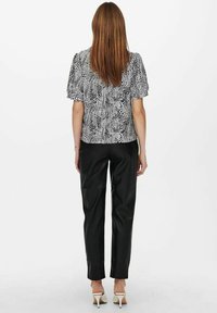 Blouse à manches courtes noire et blanche à motif avec un col rond, assortie à un pantalon noir ajusté et des chaussures à talons blanches.