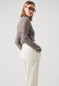 Haut gris transparent avec un motif à carreaux, associé à un pantalon blanc taille haute, doté d'une texture lisse et de poches latérales.
