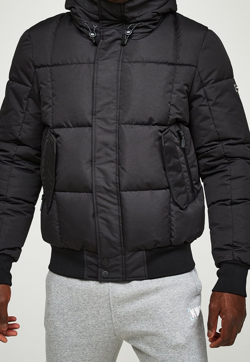 Sort dunjakke med hætte, lynlåslommer og quiltet design. Materiale i bomuldsblanding med ribstrikkede manchetter og kant.