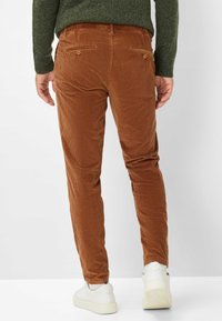 Pantaloni in velluto a coste marroni con una texture a coste verticali, slim fit, e tasche posteriori con bottoni. Indossati con sneakers bianche.