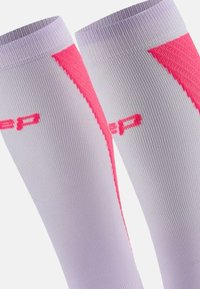 Calze compressive bianche con accenti rosa audaci. Presentano una texture rigata e una finitura liscia. Logo in rosa stampato sul tessuto.