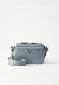 Lyseblå rektangulær crossbody-veske i strukturert skinn, med frontlomme med glidelås, sølvfarget metallbeslag og justerbar stropp med logo.