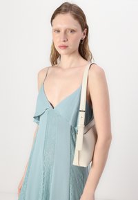 Svetlo modra obleka z čipkastimi detajli, gladka silhueta in tanke naramnice. Poudarjena z majhno kremasto torbico s trakom.