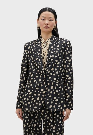 Black blazer with large beige polka dots, single-breasted design, notched lapels, and two front pockets. Paired with a beige polka dot shirt.