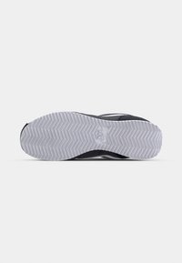 Černá a šedá sportovní podrážka s herringbone vzorem, obsahující bílé logo blízko paty a texturovaný gumový materiál.