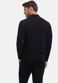 Schwarzer Strickpullover mit hohem Kragen, langärmlig und mit geripptem Saum. Glatte Textur mit taillierter Passform, schlicht, ohne Verzierungen.