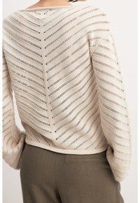 Pitkähihainen beige virkattu neule avoimella, vinoraitakuvioinnilla. Pintastruktuuri. Yhdistetty oliivinvihreisiin housuihin, joissa on rento istuvuus.