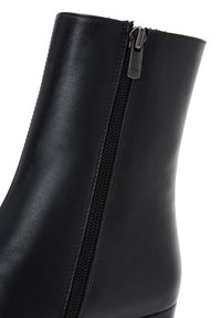 Botas de tobillo de cuero negro con cremallera lateral, textura suave y un diseño ajustado. El caña tiene un borde superior limpio y redondeado.