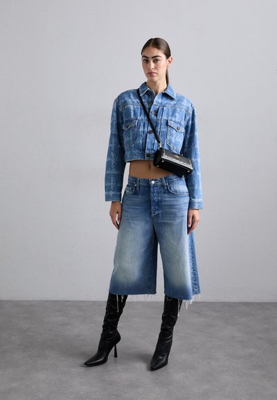 Krčen modri kavbojki jopič z subtilnimi vzorci, svetle modre kavbojke culottes z visokim pasom in črne čevlje z visokimi petami, ki poudarjajo moden videz.