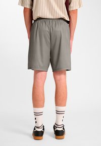 Grå träningsshorts med resårmidja, slät yta och sidofickor, kombinerade med randiga vita och grå strumpor samt svarta skor.