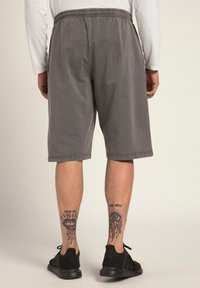 Shorts grises en coton avec une taille élastique, coupe à mi-cuisse et ourlets double couture. Portés avec des chaussures de sport noires.
