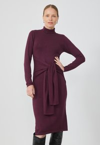 Langsleeves, bordeaux gebreide jurk met een hoge halslijn en een strikdetail aan de voorkant bij de taille. Aansluitende silhouet, reikt tot onder de knie.