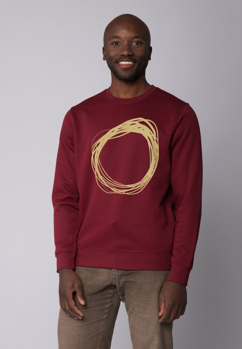 Sweat-shirt bordeaux avec un design circulaire doré au centre. Il a des manches longues et un col rond côtelé. Texture lisse, coupe décontractée.