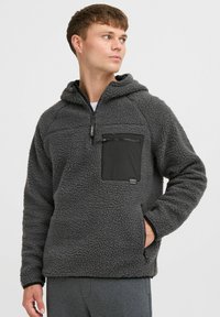 Grijze fleece pullover hoodie met een gestructureerd oppervlak, een zwarte ritszak op de borst en contrasterende zwarte afwerking op de manchetten en de kraag.