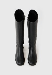 Botas de couro pretas até ao joelho com um acabamento suave, biqueira quadrada e fecho com zíper lateral. Parte superior texturizada e forro macio.