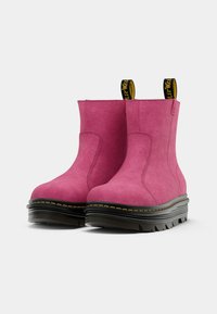 Pink suede ankle boots with a chunky black sole and yellow accents. Features a pull tab for easy wear and textured material.