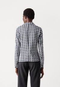 Blazer a righe navy e bianche con colletto e maniche lunghe. Il tessuto presenta un design geometrico. Vestibilità sartoriale con dettaglio della cucitura sul retro.
