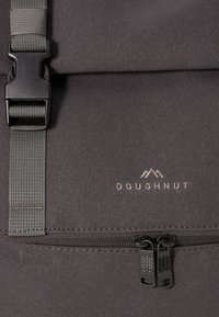Juodas audinio kuprinės su tekstūruota paviršiumi, pasižyminčios kontrastinga pilka juosta, dvipusiu užtrauktuku ir minimalistiniu logotipu.