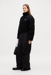 Svart kort pufferjakke med fleece tekstur, høy krage og brystlomme. Kombinert med løstsittende svarte cargo bukser og kraftige svarte støvler.