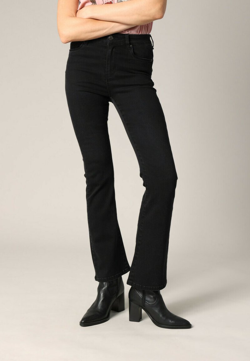 Jeans flare en denim noir à taille haute, avec un design classique à cinq poches et des détails de couture subtils. Associés à des bottes à talons noires.