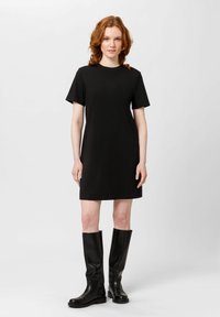 Černé šaty s krátkým rukávem volného střihu, vyrobené z měkké bavlněné tkaniny, v kombinaci s vysokými černými koženými botami pro elegantní vzhled.