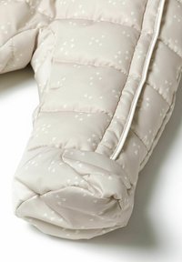 Parka rembourrée de couleur beige clair avec un motif géométrique de petits triangles blancs. Elle présente une texture lisse et une fermeture éclair blanche en contraste.