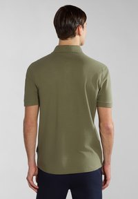 Polo shirt verde oliva con una texture morbida, maniche corte e colletto classico. Presenta un orlo dritto e spacchetti laterali.